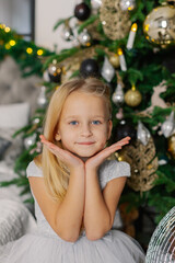 Beautiful little girl sitting by the Christmas tree.