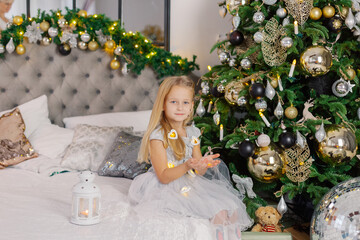 Beautiful little girl holding Christmas candles in her hands while sitting on the bed.