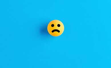 Sad face emoticon or icon on a ball on blue background. Negative feedback