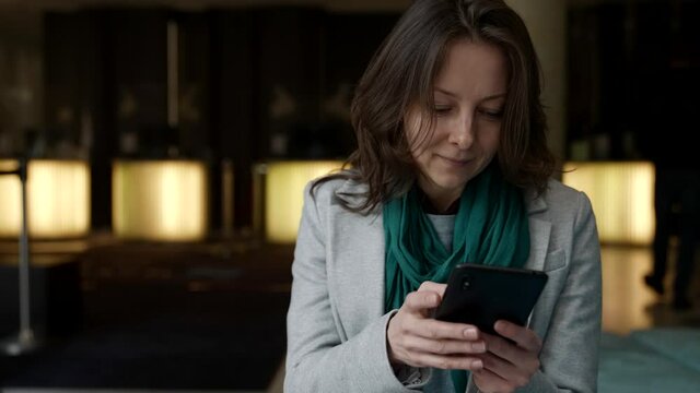 A Happy Businesswoman Searches For A Mobile Phone In The Hotel Lobby. Portrait Of A Smiling Businesswoman Reading A Mobile Message On The Phone In A Cafe