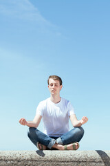 Naklejka na ściany i meble Young man meditating in lotus pose outdoors in a sunny day.