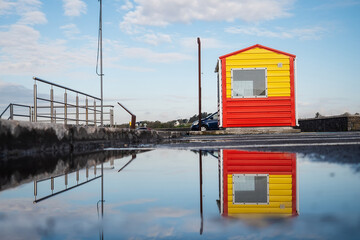 Yellow and red life guard station with sky reflection in a puddle of water. Rich blue cloudy sky. Low angle of view