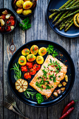 Roasted salmon steak with roast potatoes and vegetable salad served on black plate on wooden table
