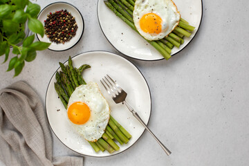 Homemade asparagus with fried egg on white plate, top view, light grey background. Copy space.