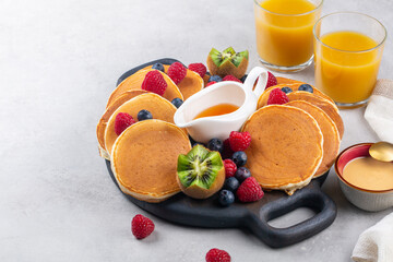 Breakfast table. Orange juice with pancake board: homemade pancakes, honey, kiwi, peanut butter, fresh fruits: raspberries, blueberries, Light grey background. Close-up.