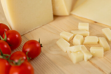 set photo of a typical Italian light-colored cheese, placed on a wooden cutting board, and cut into cubes. around there are rosemary, peppercorns, tomatoes, chilli