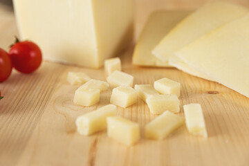 set photo of a typical Italian light-colored cheese, placed on a wooden cutting board, and cut into cubes. around there are rosemary, peppercorns, tomatoes, chilli