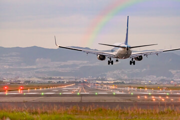 虹のかかる空を背景に着陸する飛行機