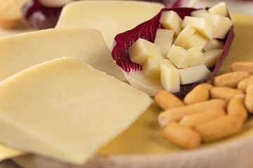 photo of the detail of a typical Italian light-colored cheese, arranged on a wooden cutting board, and cut into cubes inside a salad leaf. high definition image, for magazines, social networks, websit