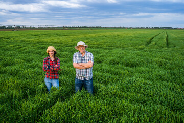 Proud two generations farmers are standing in their barley field in sunset. - obrazy, fototapety, plakaty