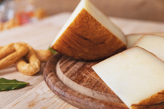 photo of slices of a typical Italian light-colored cheese, arranged on a dark wooden cutting board. around there are bay leaves, chilli and Apulian croutons. HD image for magazines, sites, social netw