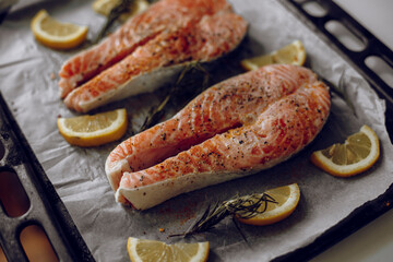 salmon steaks on a baking sheet. chunks of salmon seasoned with pepper along with lemon wedges and rosemary. ready-to-cook pieces of red fish. cooking seafood for two.
