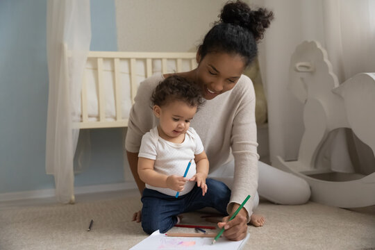 Smiling African American mother have fun enjoy drawing painting with cute small toddler daughter child. Happy biracial mom feel playful relax with little baby girl kid. Parenthood concept.