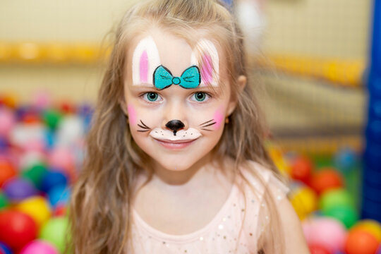 beautiful girl with face painting - a multi-colored hare drawn with paints, in the children's playroom