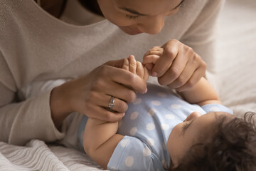 Close up of young African American mother cuddle play with little newborn baby girl child at home...