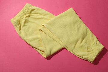 Folded yellow sweatpants on pink background, top view