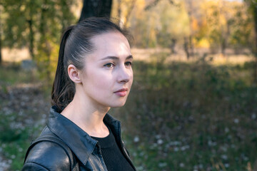 Portrait of girl on park background. Beautiful brunette young woman thoughtfully looks straight. Side view.