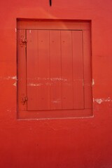 Painted wooden window shutter in a matching red wall with a few scuffs vertical architecture background