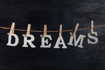 Fototapeta premium Word DREAMS with clothespins on black background. Dream visualization