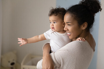 Smiling young African American mother hold in arms look in distance dream with cute little baby daughter. Happy biracial mom visualize imagine play with small toddler girl child. Parenthood concept.