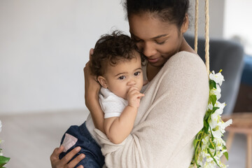 Happy caring young African American mother hold cuddle caress small ethnic baby daughter child....