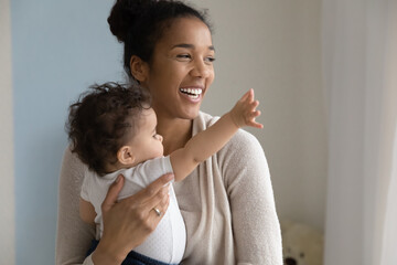 Overjoyed young African American mother hold in arms play with cute little baby daughter at home....