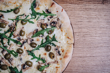 Appetizing Pizza on a wooden table in a restaurant. Close-up of melted cheese, olives, mushrooms, and herbs. Freshly cooked cheese pizza on a wooden board. Italian cuisine.