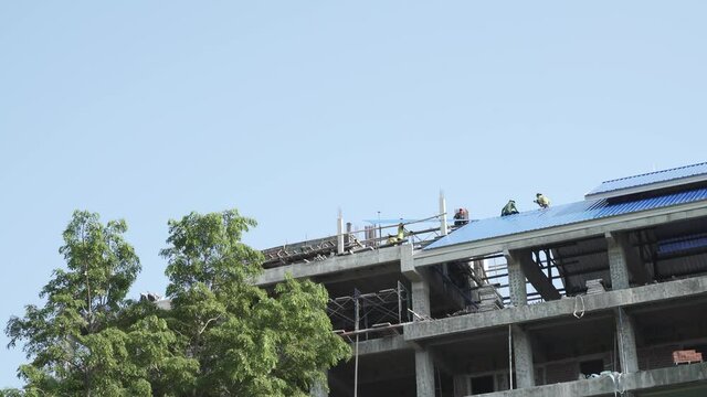 Asian worker building new stainless steel metal sheet roof for a public school in Thailand