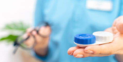 Close-up of a female doctor holding a pair of contact lenses and glasses. Ophthalmologist give recommendations on choice of vision correction and eye health to a patient in an optics store or clinic