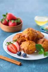 Healthy vegan carrot muffins with cinnamon, honye, mint leaves, strawberry and blueberry on white plate. Blue stone background. Vertical irientation, copy space.