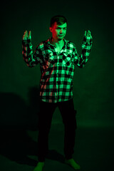 A young man in a plaid shirt in a studio with red and green light on a black background