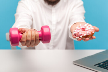 Closeup bearded man holding out hands with pink dumbbell and sweet donut with icing to camera...