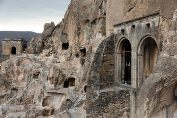 Complex of Vardzia cave monastery structures carved on mountain slope with view of temple of Assumption of Blessed Virgin Mary with deepened into rock arches of narthex and bells, Javakheti, Georgia