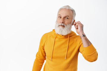 Did you say something. Senior hipster man take-off earbud to hear you. Old stylish guy looking questioned, cant hear you while listening music in headphones, white background