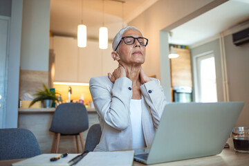 Cropped shot of a mature businesswoman looking stressed out while working in her office at home. Mature businesswoman having neck pain. Stressed mature woman massaging her neck. - obrazy, fototapety, plakaty