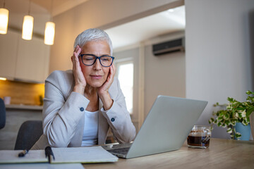 Upset, unhappy, pretty, charming, professional teacher feeling bad, took off glasses, touching her temple, suffering from headache, sitting at desk in workstation, having computer, tablet on the table