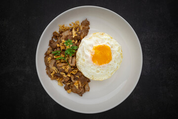 Khao Moo Tod Kratiam Kai Dao, Thai food, streamed rice topped with fried pork with garlic and fried egg in ceramic plate on dark grey texture background