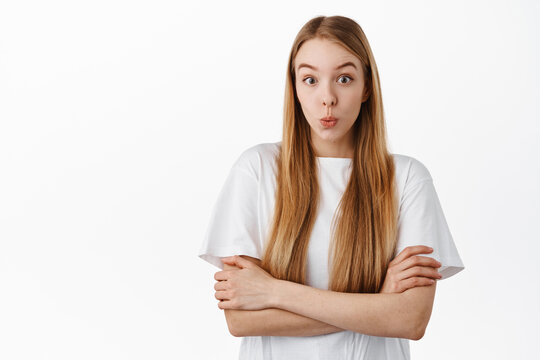 Image of young woman in t-shirt, cross arms on chest and looks surprised, say wow, stare with curious and excited face, checking out something cool, standing over white background
