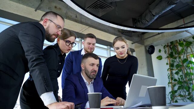 Happy business people looking at laptop presentation, success at work, sitting in modern office. Successful online negotiations. Businessmen share their knowledge