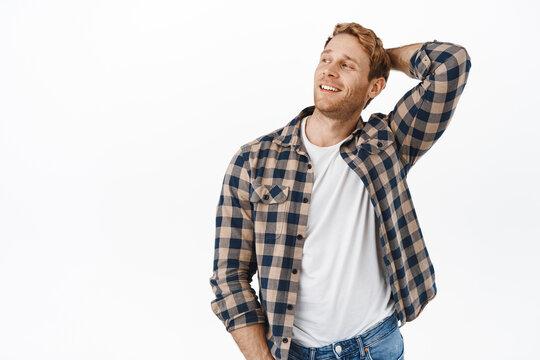 Image of handsome and confident macho man with red hair and strong arms, holding hands behind head, looking aside and smiling satisfied, resting, relaxing against white background