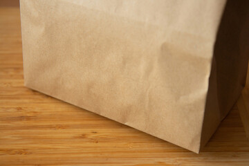 Brown craft paper bag on light wooden background. Recycled paper shopping bag, lunch bag