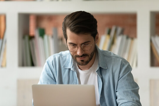 Close up confident businessman in glasses working on laptop, looking at computer screen, reading business email, chatting in social network, focused student watching webinar, browsing apps