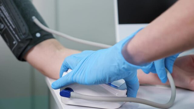 Nurse puts cuff on man patient arm to measure pressure with digital tonometer sitting at table in hospital office extreme close view
