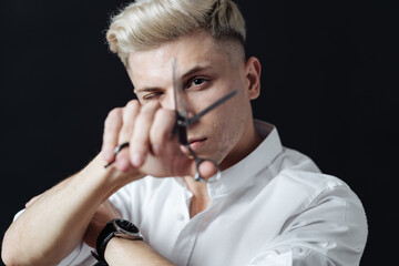 Portrait of blond male in white shirt stylist holding scissors near face over black background.