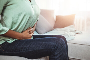 Woman lying on sofa looking sick in the living room. Beautiful young woman lying on bed and holding hands on her stomach. Woman having painful stomachache on bed, Menstrual period