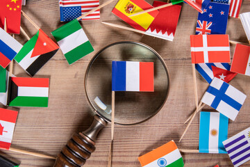 Fototapeta premium French flag and magnifying glass. Business opportunities, travel, politics and research concept. Flags of different countries on a wooden background