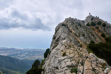 Group of hikers climb a rocky mountain with the sea in the background and clouds near the climbers