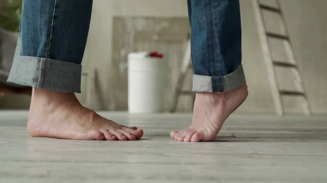 A barefoot woman standing on tiptoe on the floor hugs and kisses a man at home, a young couple stands in their house where repairs are underway