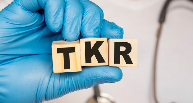 TKR Total knee replacement - word from wooden blocks with letters holding by a doctor's hands in medical protective gloves. Medical concept.