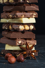 Stack of milk and dark chocolate with nuts, caramel and fruits and berries on dark marble background..